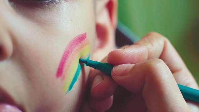 Close-up view of a little boy. LGBTQ parent painting rainbow flag on cheeks. Pride day 2020, LGBT family, gender rights and equality concepts