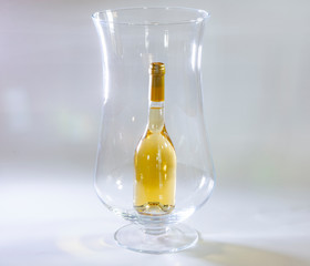 Small bottle of white wine inside a huge wine glass