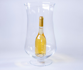 Small bottle of white wine inside a huge wine glass