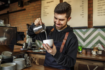 Smiling bearded barista pouring milk in a cup at the coffee shop