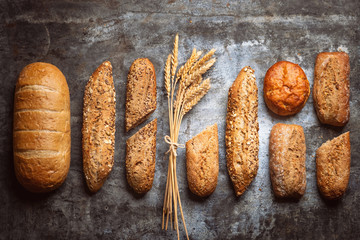 Fresh bakery food. Crusty loaves of mixed breads and buns and ears of wheat on rustic table background. Top view and copy space for your advertising text message