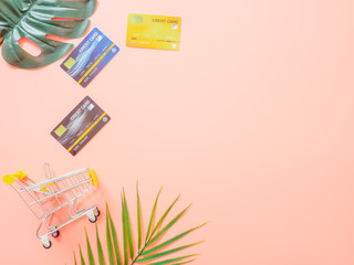 Summer shopping and payment concept from credit cards or discount cards and small trolley on pastel pink background.