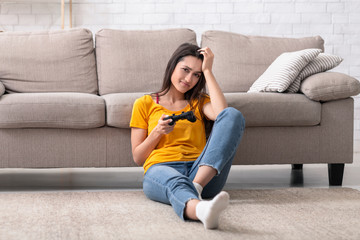 At home pastimes. Young woman with controller sitting on floor upset, losing video game © Prostock-studio
