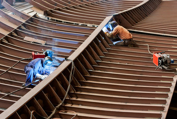 Professional shipbuilders working with a safety helmet, welding parts of a new ship's hull