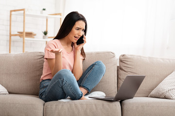 Obraz premium Frustrated woman talking on mobile phone sitting on sofa