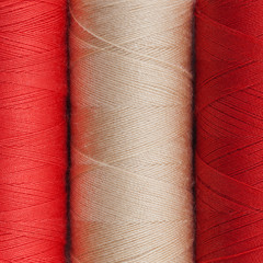 beautiful background of three spools of cotton thread of bright contrast colors - red and white