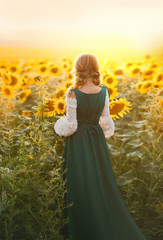 Young rural woman peasant turned away. Bavarian beauty green vintage medieval national dress costume. Hairstyle blonde two braids. Girl walks in blooming field, yellow flowers sunflower, summer nature