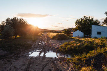 Sunset in the Spanish countryside next to a farmhouse on a path with puddles in spring.