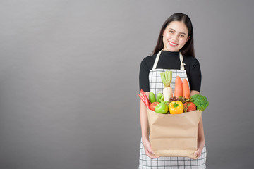 Portrait of beautiful young woman with vegetables in grocery bag in studio grey background