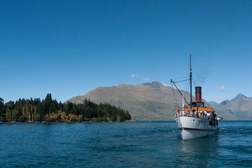 Steam ship coming across the lake with mountains and trees behind