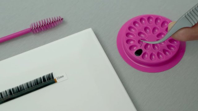 A lash technician or beautician making a Russian volume lash fan and dipping it into adhesive.  A beauty professional demonstration of lash extensions treatment