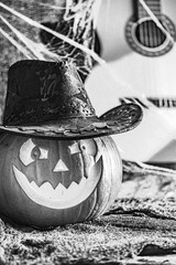 Black and white,  slightly blurred photo with strong grain effect. Laughing pumpkin in cowboy hat with guitar in the background. Halloween,  artistic concept.