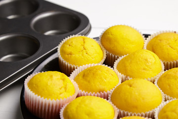 Cupcakes on black plate, baking tray on white wooden table. Pumpkin muffins. Homemade bakery