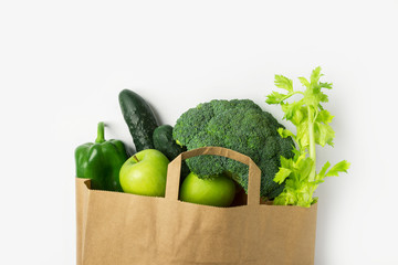 Green raw organic vegetables fruits broccoli cucumbers bell peppers apples celery in brown paper grocery bag on white background. Healthy diet online food shopping delivery plastic free concept