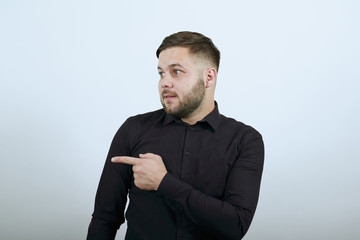 Young Bearded Dark Haired Man In Black Stylish Shirt On White Background, Confused Male Shows...