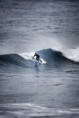 Surfer in full wetsuit and hood surfing a cold looking wave, Cornwall, UK