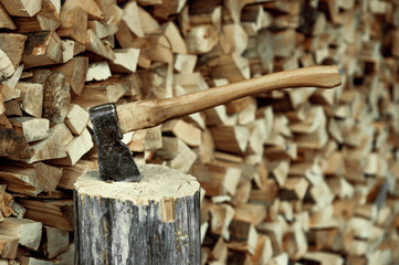 A large old ax sticks out of a wooden hemp block against a background of firewood.