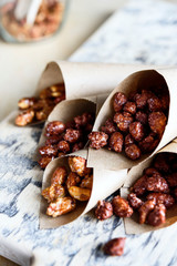 Caramelized sugared peanuts in paper envelope bags on wooden background. Selective focus