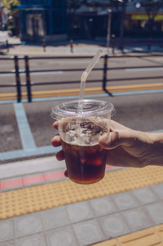 man holding plastic mug of iced convinience store coffee