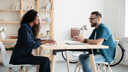 Happy hr manager laughing interviews new african american applicant using resume and laptop. Smiling businessman in negotiation with attractive diverse woman job seeker in office at hire meeting.