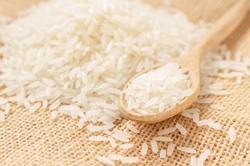 Close up raw rice grain on wooden spoon and sack cloth