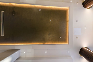 look up on suspended ceiling with halogen spots lamps and drywall construction with fire alarm sensor in empty room in apartment or house. Stretch ceiling white and complex shape.