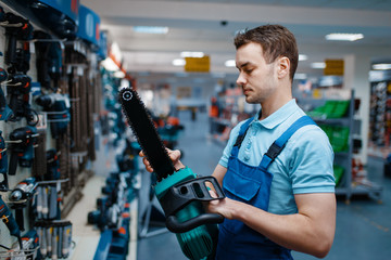 Worker in uniform holds electric saw in tool store