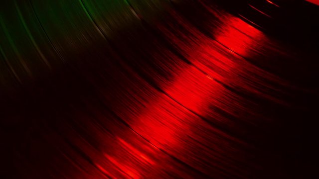 A fragment of a rotating vinyl record in the red rays of a disco. Audio equipment for dj. The moment of a spinning vinyl plate. Turntable vinyl record player