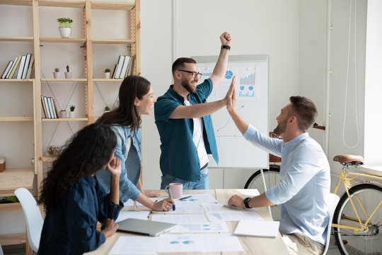 Businessman leader, coach giving high five to colleague at company meeting. Man with diverse corporate group celebrating achievement, corporate success of teamwork, team building activity.