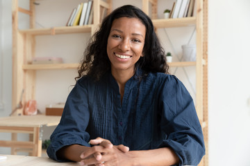 Close up headshot portrait picture of happy african american businesswoman sitting by table. Smiling attractive young diverse woman mentor looking at camera in coworking office.