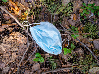 Medical face mask thrown away in city forest laying on the leaves and grass among the fresh green sprouts of trees or bushes