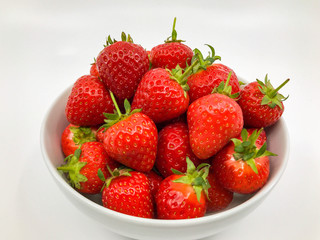 Plump ripe fresh strawberries in a white bowl on a plain white background.