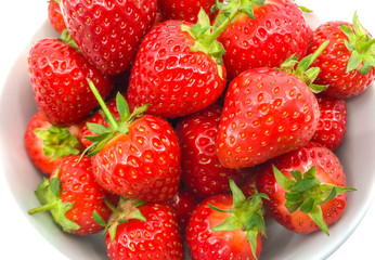 Close up of plump ripe fresh strawberries in a white bowl on a plain white background.