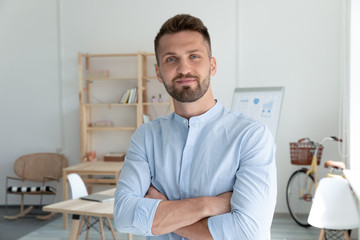 Obraz premium Close up head shot portrait picture of smiling businessman crossing hands looking at camera. Happy confident millennial man manager on workplace background in office.