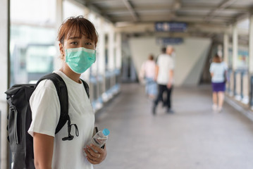 Asian woman with surgical face mask feel tired standing on skywalk after travel by skytrain, carrying backpack,  traveling to the city, social distancing, coronavirus, COVID19