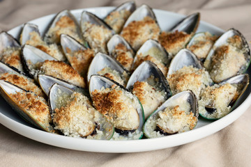 Mussels baked with parmesan, bread crumb and herb butter served on a plate. Food background. Mediterranean cuisine. Concept for a tasty and healthy meal. Close up.