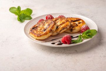 Homemade cheesecakes with raspberries, syrup and mint on a ceramic plate on a light wooden background. Copy space for text