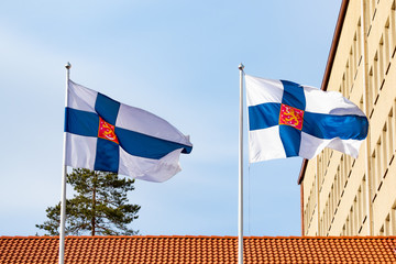 Two finnish national flags with coat of arms on the wind against the blue sky
