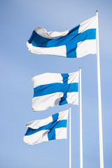 Obraz premium Three finnish national flags on the wind against the blue sky