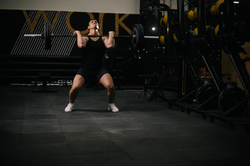 Obraz na płótnie Canvas Athletic muscular man with perfect beautiful body wearing sportswear lifting heavy barbell from floor during sport workout training in modern dark gym. Concept of healthy lifestyle.