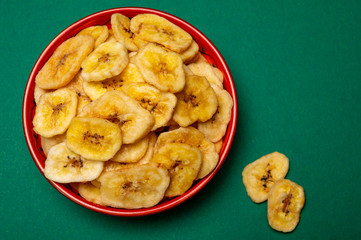 Healthy snack, crispy dehydrated unsugared banana chips in bowl on green background