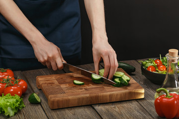 Woman cooking fresh healthy salad. Female hands cutting vegetables on board on wooden table with copyspace.