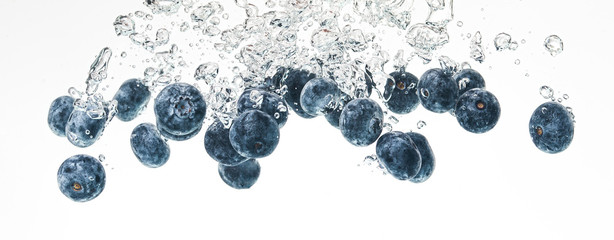 Blueberries sinking into water with air bubbles on white background.