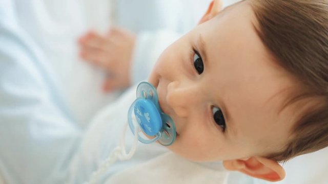 Close up of nice caucasian newborn baby on the bed and sucking a pacifier