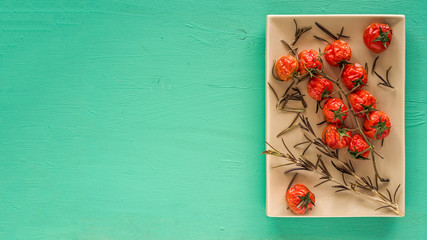 Baked cherry tomatoes and rosemary sprigs on an emerald background. Top view. Copy space.