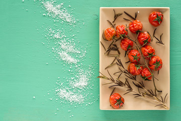 Grilled cherry tomatoes and rosemary on emerald background with copy space.