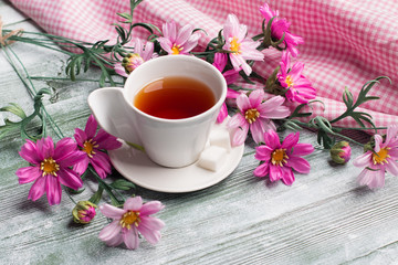 Artificial cosmos bipinnatus and cap of tea on green wood table