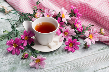 Artificial cosmos bipinnatus and cap of tea on green wood table