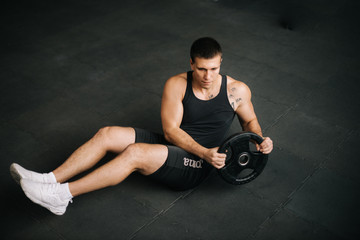 Muscular strong man doing russian twist exercise with weight from barbell on black mat during sport...