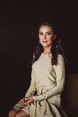 A beautiful young dark woman with dark curly hair and brown eyes in a gold dress sits on a mustard sofa in the loft room. Soft selective focus.